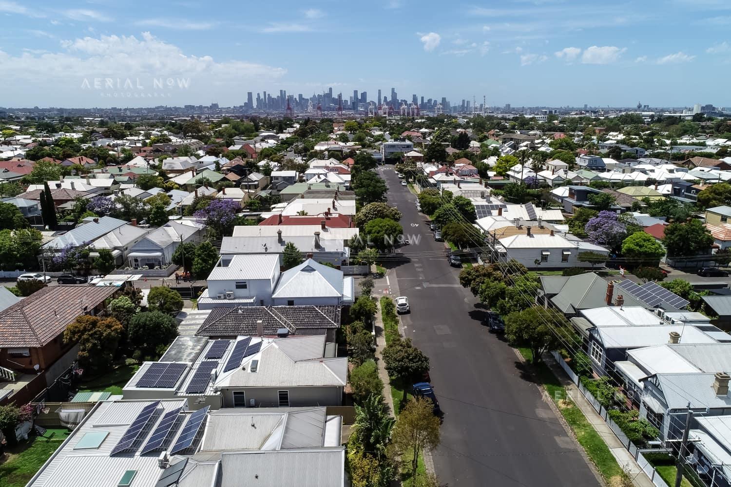 Aerial view over residential streets and rooftops in Yarraville, with the Melbourne CBD skyline visible in the background.