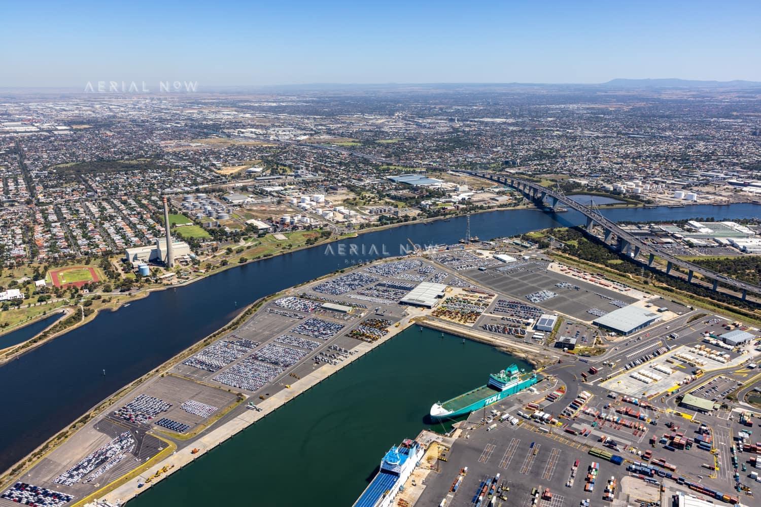 Aerial view of Webb Dock West vehicle storage and roll-on roll-off berths beside the Yarra River in Port Melbourne, with the West Gate Bridge and Melbourne suburbs beyond.