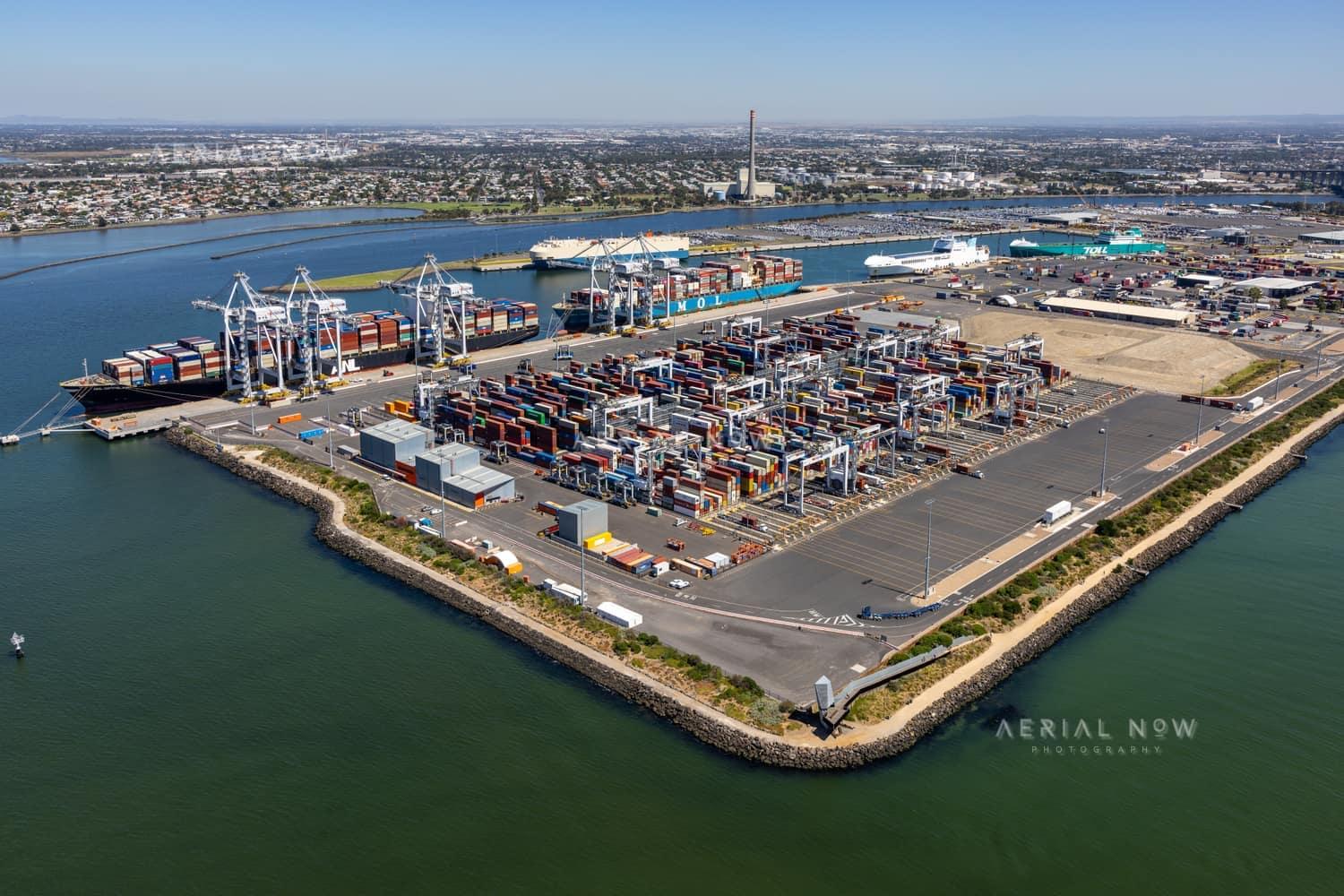 Aerial view of Webb Dock East container terminal at Port Melbourne in February 2022, with container stacks, ship-to-shore cranes, working berths and Port Phillip Bay.