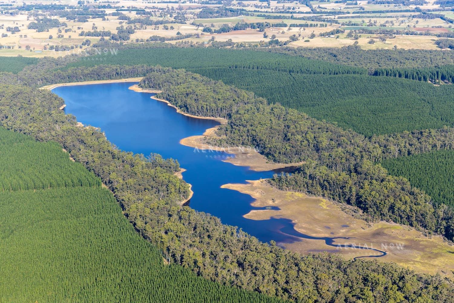 Aerial view of Bostock Reservoir at Spargo Creek, with blue water, exposed shoreline, surrounding native bushland and pine plantations.