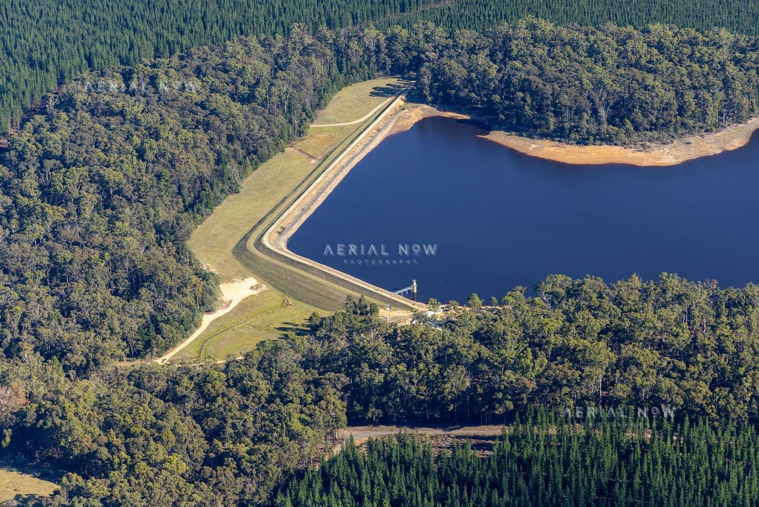 Aerial view of Bostock Reservoir at Spargo Creek, showing the earth embankment, access road, outlet structure, dark water and surrounding forest.