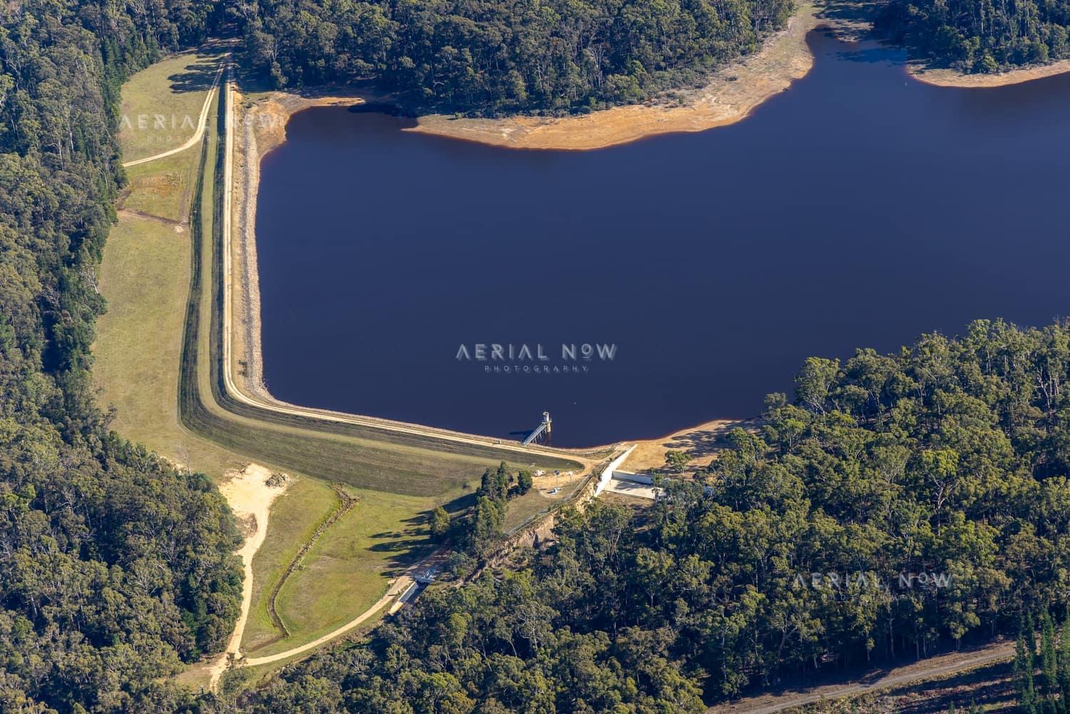 Aerial view of Bostock Reservoir at Spargo Creek, showing the dam embankment, dark water, exposed shoreline and surrounding forest.
