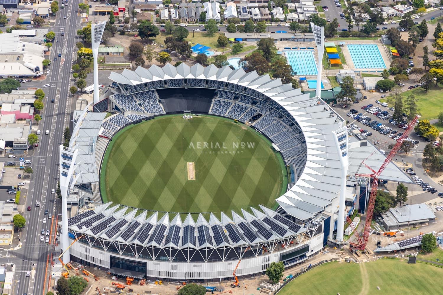 Aerial view of GMHBA Stadium at Kardinia Park in South Geelong, showing the oval, grandstands, light towers, nearby Moorabool Street, aquatic centre pools and construction activity.
