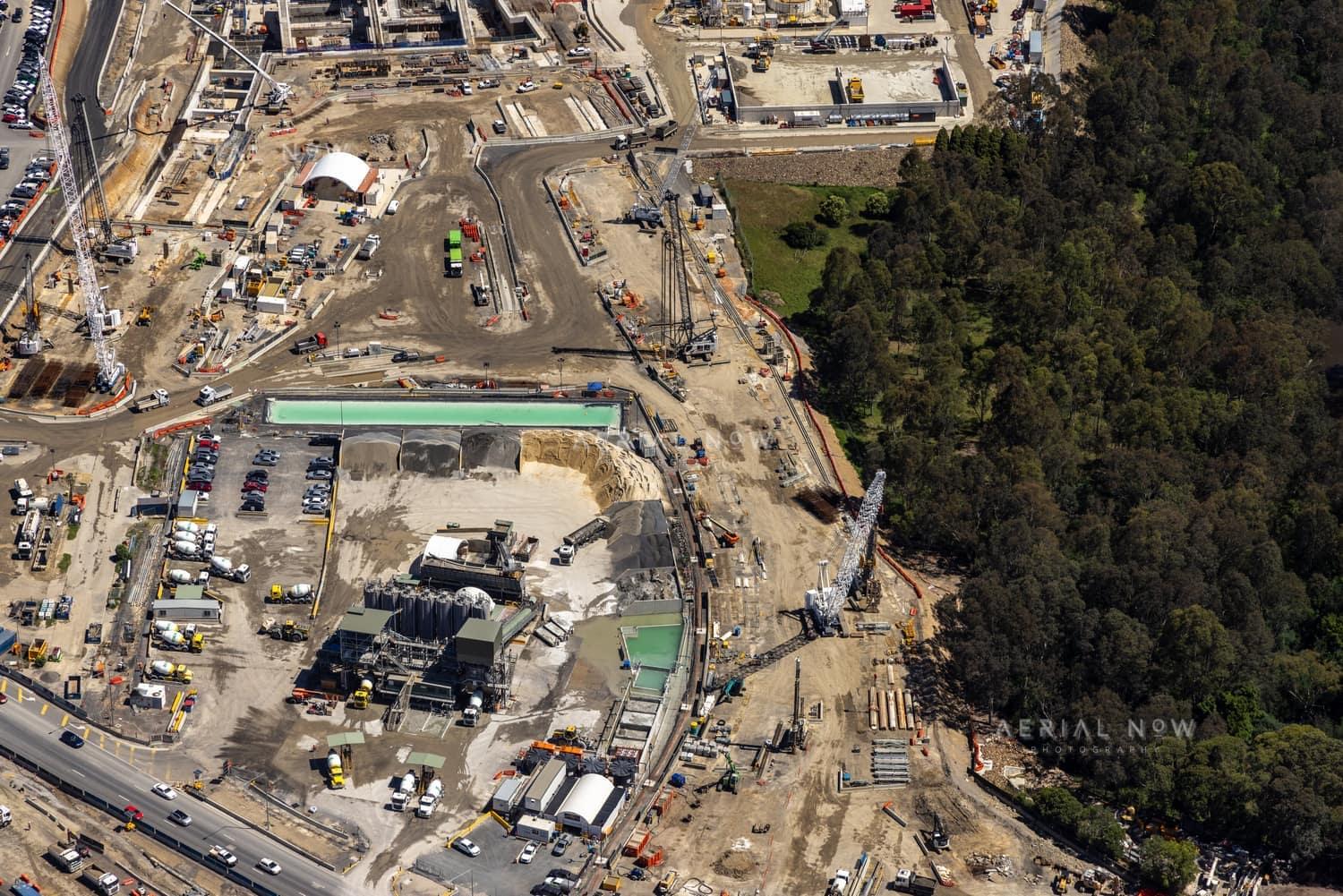 Aerial view of the North East Link construction compound in Bulleen, with cranes, earthworks, equipment yards and adjacent bushland.