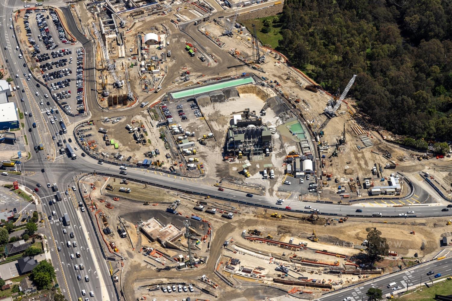 Aerial view of North East Link construction works in Bulleen, with major roadworks, cranes, machinery, site compounds and traffic on surrounding arterial roads.