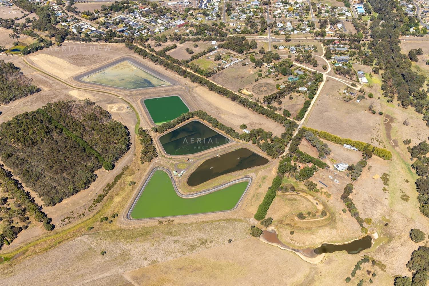 Aerial view of wastewater treatment ponds and service tracks on the edge of Winchelsea, VIC, with rural paddocks and township streets nearby.