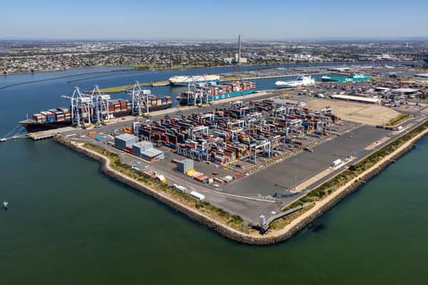 Aerial view of Webb Dock East container terminal at Port Melbourne in February 2022, with container stacks, ship-to-shore cranes, working berths and Port Phillip Bay.