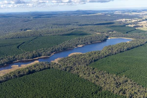 Aerial view of Bostock Reservoir with a narrow shoreline surrounded by dense forest and plantation land near Bolwarrah, Victoria.