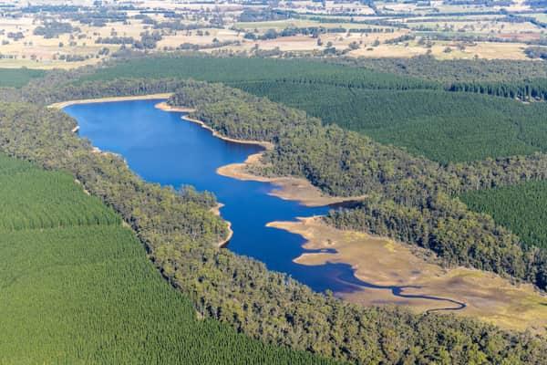 Aerial view of Bostock Reservoir at Spargo Creek, with blue water, exposed shoreline, surrounding native bushland and pine plantations.