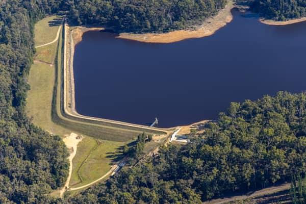Aerial view of Bostock Reservoir at Spargo Creek, showing the dam embankment, dark water, exposed shoreline and surrounding forest.