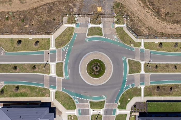 Aerial view of a landscaped roundabout with bike lanes, pedestrian crossings, footpaths and surrounding residential lots in Mickleham, Victoria.
