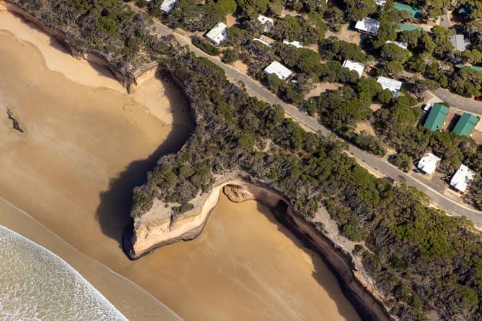 Aerial view of Point Roadknight in Anglesea, showing sandy beach, eroded coastal bluffs, vegetated clifftop and nearby houses along Lubel Street.