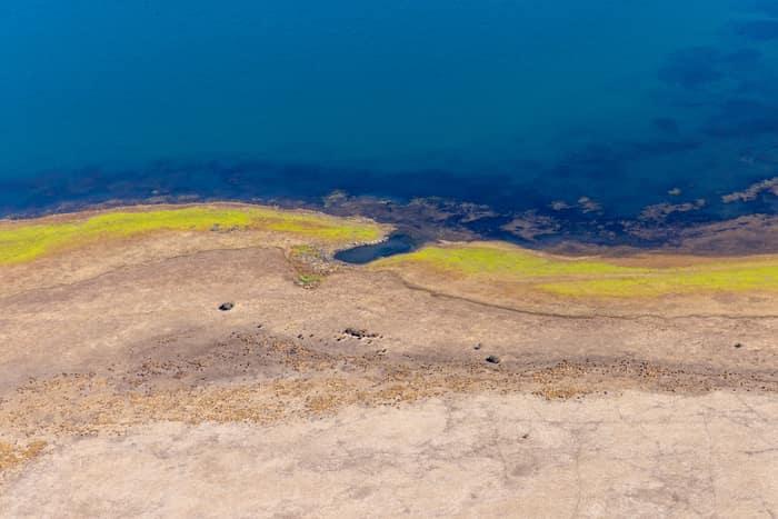 Aerial view of Lake Modewarre shoreline at Modewarre VIC, showing blue water, exposed lakebed and yellow-green vegetation along the shallow edge.