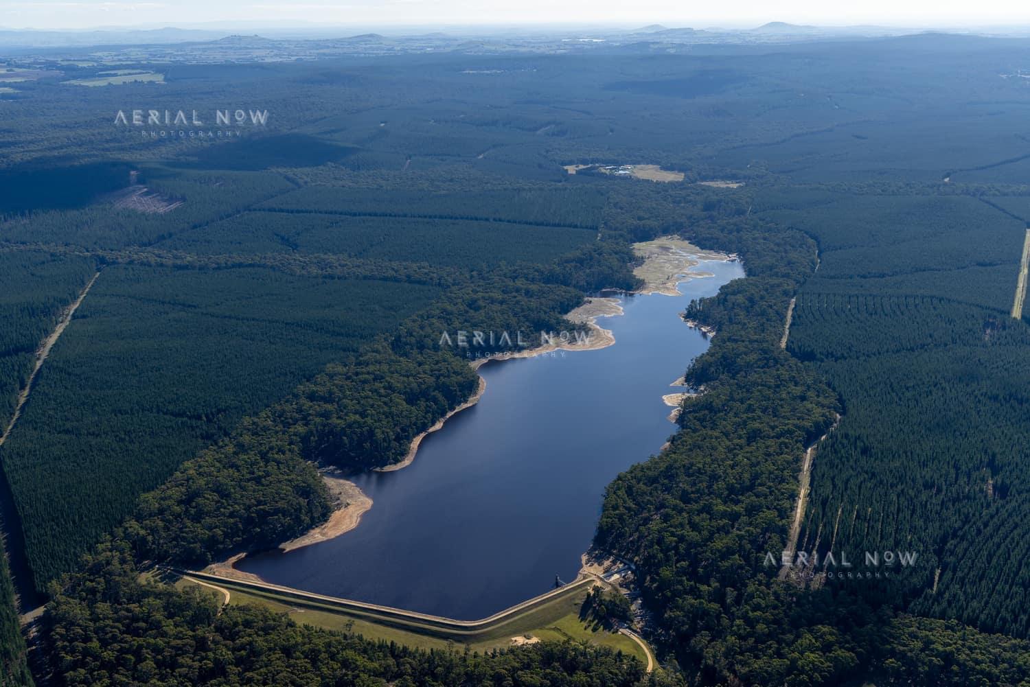 Aerial view of Bostock Reservoir in Bunding, Victoria, showing the dam wall, curving shoreline and surrounding forest plantations.