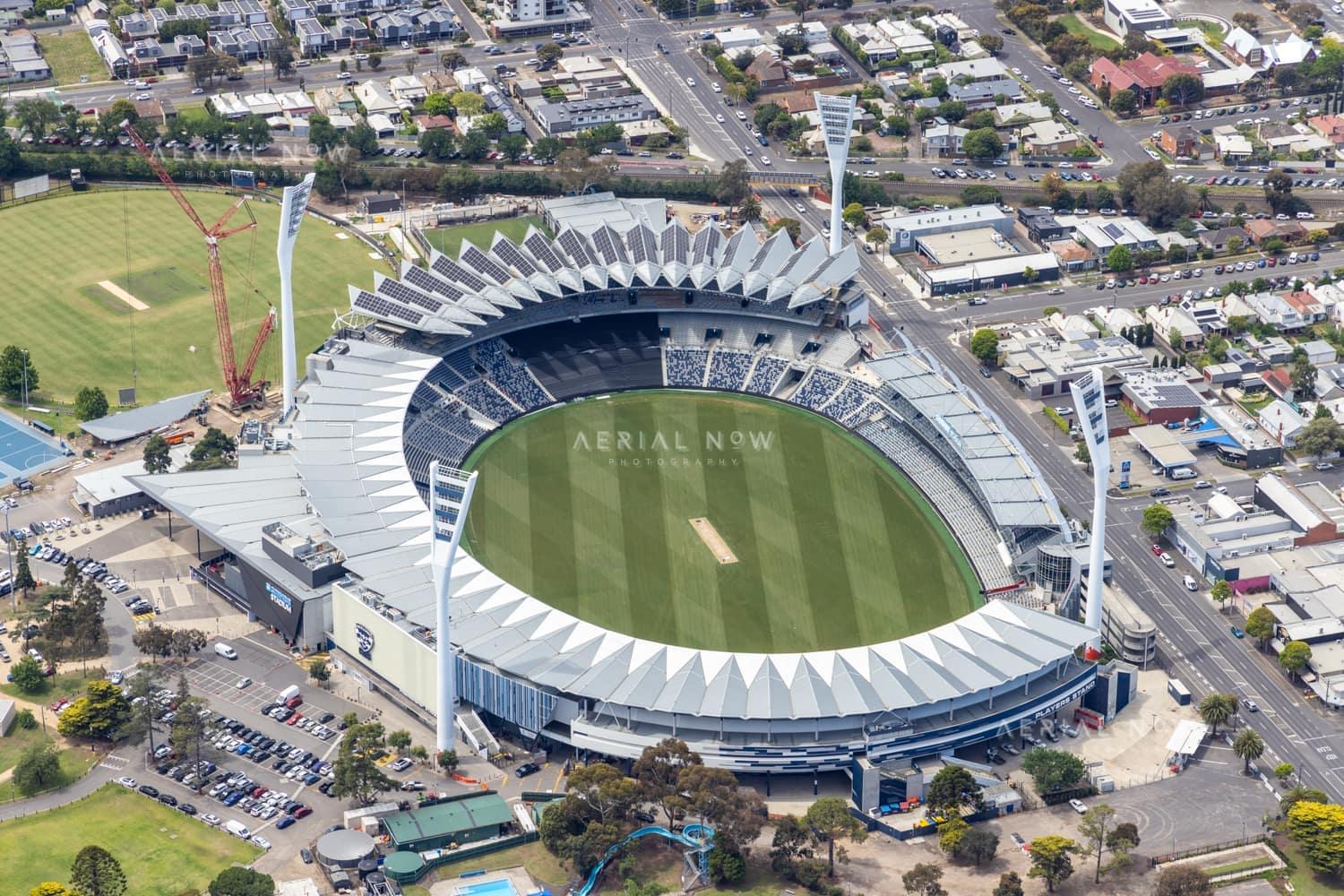 Aerial view of GMHBA Stadium at Kardinia Park in South Geelong, showing the oval, grandstands, light towers, surrounding streets and cranes near the precinct.