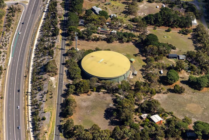 Aerial view of a large circular water storage tank beside Andersons Road in Drysdale, with nearby rural properties, trees and a divided road corridor.