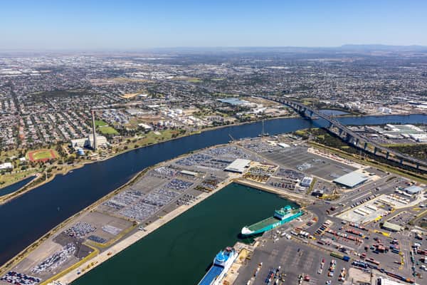 Aerial view of Webb Dock West vehicle storage and roll-on roll-off berths beside the Yarra River in Port Melbourne, with the West Gate Bridge and Melbourne suburbs beyond.