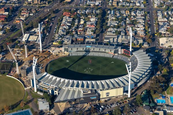 Aerial view of GMHBA Stadium at Kardinia Park in South Geelong, showing the oval, seating bowl, light towers and a construction zone with cranes beside one stand.