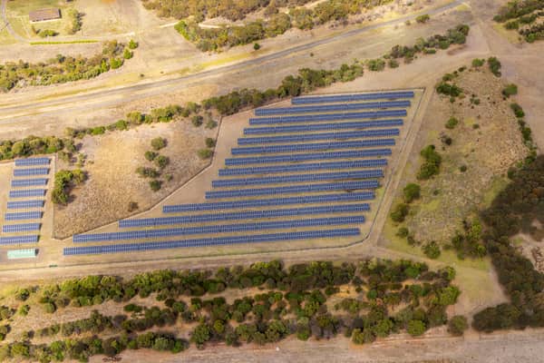 Aerial view of Black Rock Solar Farm in Connewarre, with rows of photovoltaic panels set among dry grassland, trees and access tracks near the Black Rock Water Reclamation Plant.